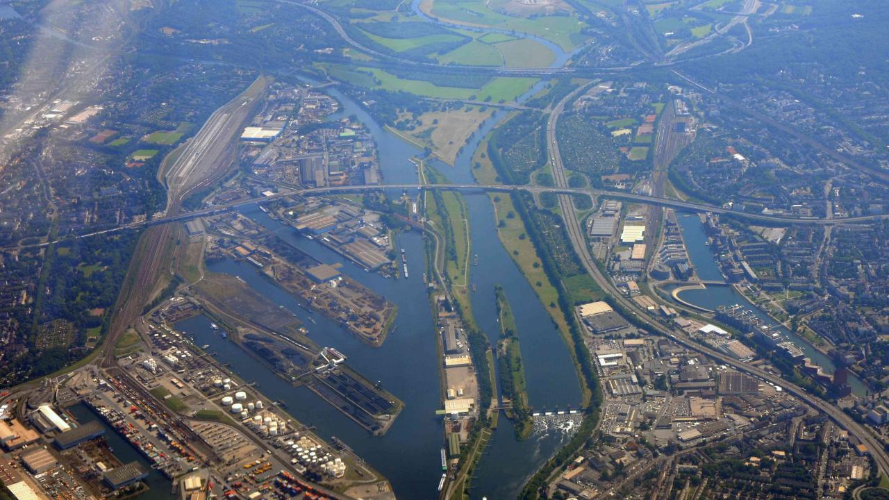 Luftbild aus großer Höhe auf einen breiten Flusslauf und abzweigende Hafenbecken, Bebauung, Straßen, Grünflächen, Wald