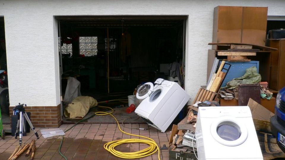 Garageneinfahrt eines Hauses vor dem kaputte Hausshaltsgeräte und Möbel aufgestapelt sind, Schlauch