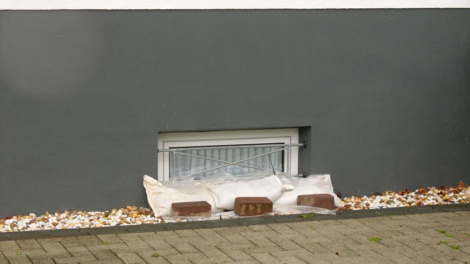 gepflasteres Grundstück und Hauswand mit einem Kellerfenster, Sandsäcke und Ziegelsteine