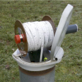 Auf dem Foto ist ein aufgerolltes Maßband zu sehen, dass in ein Rohr an einer Grundwassermessstelle hineinreicht.